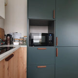 Een moderne keuken met yessential.nl's Lucasso Walnut handgrepen, groene kasten, een ingebouwde magnetron en een houten aanrecht met potten en keukengerei - een perfecte touch voor een natuurlijke inrichting.
