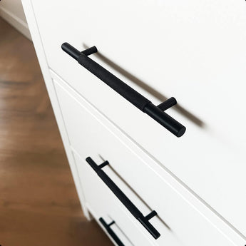 Close-up van witte lades met yessential.nl Remo Black Deluxe meubelgrepen, voorzien van luxe structuurgrepen, tegen een achtergrond van een houten vloer.