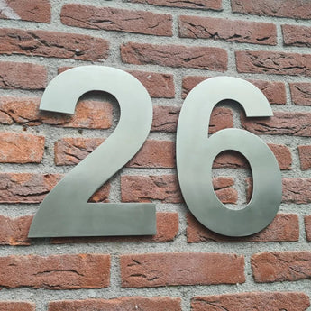 Grote Adamo RVS 30cm nummers van yessential.nl zijn gemonteerd op een rode bakstenen muur en dienen als prominent huisnummer voor duidelijke gebouwidentificatie.