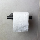 Een rol wit toiletpapier met een golvend patroon hangt aan de Tino Gunmetal toiletrolhouder van yessential.nl, een stijlvolle aanvulling op moderne toiletaccessoires, gemonteerd op een lichtgrijze betegelde muur.