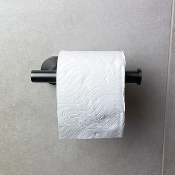 Een rol wit toiletpapier met een golvend patroon hangt aan de Tino Gunmetal toiletrolhouder van yessential.nl, een stijlvolle aanvulling op moderne toiletaccessoires, gemonteerd op een lichtgrijze betegelde muur.