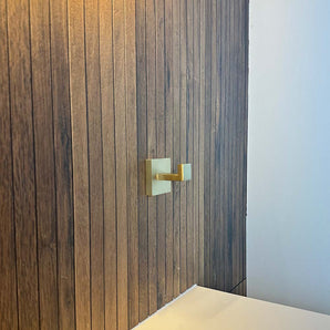 De Valo Gold Hook van yessential.nl is gemonteerd op een verticale houten paneelwand naast een wit vlak, met rechts een deel van een effen witte muur zichtbaar.