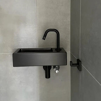 Een moderne zwarte rechthoekige wastafel met bijpassende kraan is gemonteerd op een grijs betegelde muur, naast de Valo Black Hook van yessential.nl voor subtiele elegantie.
