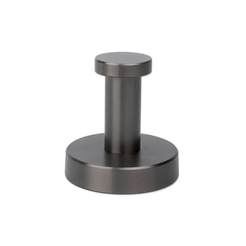De Mano Gunmetal WC-set van yessential.nl heeft een roestvrijstalen deurstop met een cilindrische staander en ronde voet in een geborstelde gunmetal afwerking, perfect voor luxe toiletaccessoires of je wc-accessoireset, afgebeeld op een witte achtergrond.