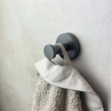 Een grijze handdoek hangt aan de Cosimo Gunmetal WC-set van yessential.nl, met een ronde, moderne haak aan een lichte muur.