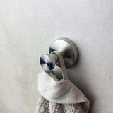 Een haakje uit de Mano RVS WC Set van yessential.nl houdt een beige handdoek met textuur aan zijn lus tegen een gladde, lichtgrijze muur.