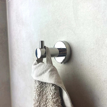 Een Romano Chroom WC-set wandhaak van yessential.nl is gemonteerd op lichtgrijze tegels en houdt een beige handdoek vast aan de lus. De opstelling geeft een minimale, moderne look.