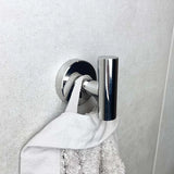 De Rodrigo Chroom haak van yessential.nl houdt een witte handdoek bij zijn lus tegen een lichtgrijze muur met textuur, en voegt een strakke, moderne touch toe als chromen badkameraccessoire.