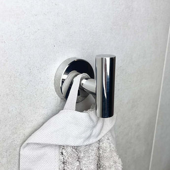 De Rodrigo Chroom haak van yessential.nl houdt een witte handdoek bij zijn lus tegen een lichtgrijze muur met textuur, en voegt een strakke, moderne touch toe als chromen badkameraccessoire.