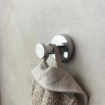 De Cosimo Chromen WC-set van yessential.nl houdt een beige handdoek met een stoffen lus tegen een lichtgrijze muur met structuur, en creëert zo een eenvoudige, minimale look die ideaal is voor verfijnde badkameraccessoires.