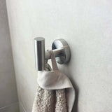 Een Rodrigo RVS haak van yessential.nl houdt een beige handdoek met textuur tegen een lichtgrijs betegelde badkamermuur.