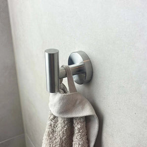 Een Rodrigo RVS haak van yessential.nl houdt een beige handdoek met textuur tegen een lichtgrijs betegelde badkamermuur.