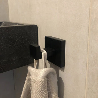 Een close-up van de Valo Black Hook van yessential.nl die een handdoek met beige textuur vasthoudt, gemonteerd op een lichte badkamermuur naast een donkere wastafel.
