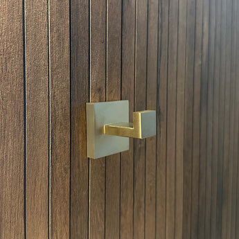 De Valo Gold Hook van yessential.nl, een goudkleurige handdoekhaak met vierkante basis, is gemonteerd op een donkerbruine houten stok met smalle panelen en is ideaal als handdoekhaken badkamer.