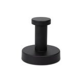 Een strakke zwarte, cilindervormige metalen deurstopper met een ronde basis en platte bovenkant van yessential.nl - een ideale match met je Xavo Black WC-set of andere matzwarte badkameraccessoires. Gefotografeerd op een witte achtergrond.