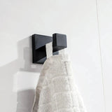 De Venzo Black WC-set van yessential.nl heeft een strak, vierkant metalen wandhaakje dat een handdoek met witte textuur vasthoudt tegen witte tegels - een ideale moderne toevoeging aan je badkameraccessoires.