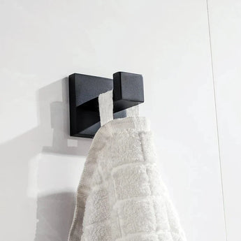 De Venzo Black WC-set van yessential.nl heeft een strak, vierkant metalen wandhaakje dat een handdoek met witte textuur vasthoudt tegen witte tegels - een ideale moderne toevoeging aan je badkameraccessoires.