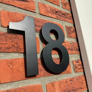 De Adamo Black 15cm huisnummers van yessential.nl zijn gemonteerd op een rode bakstenen muur met witte bies, en bieden een moderne en stijlvolle huisnummer zwart look voor je huis.