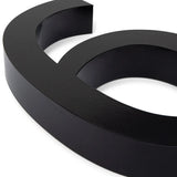 Een close-up van de Carlo Black 20cm van yessential.nl, een gestroomlijnd zwart 3D-symbool op een witte achtergrond. De gladde, glanzende afwerking doet denken aan moderne huisnummers.
