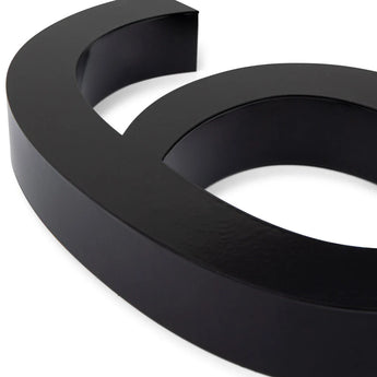 Een close-up van de Carlo Black 20cm van yessential.nl, een gestroomlijnd zwart 3D-symbool op een witte achtergrond. De gladde, glanzende afwerking doet denken aan moderne huisnummers.