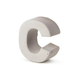 De Enrico beton 20cm van yessential.nl is een driedimensionale, lichtgrijze betonnen letter C die rechtop staat tegen een effen witte achtergrond, en benadrukt de look van een stijlvol huisnummer gemaakt van duurzaam beton.