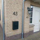 Huis met bruine bakstenen muren, nummer 43 in Amato Black 15cm huisnummer van yessential.nl, zwarte brievenbus beneden, lantaarnlamp boven en een witte deur en raam rechts.
