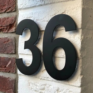 De Adamo Black 20cm van yessential.nl, met het nummer "36" in zwart op een witte bakstenen muur met rode bakstenen aan de linkerkant, is een stijlvol voorbeeld van moderne huisnummers.