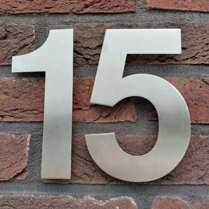 De Adamo RVS 15cm van yessential.nl is een groot metalen huisnummer 15, elegant ontworpen voor montage op een rode bakstenen muur - perfect voor wie op zoek is naar stijlvolle, duurzame huisnummers.