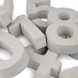 Grote, witte, driedimensionale Enrico beton 30cm cijfers van yessential.nl zijn verspreid en overlappen elkaar op een wit oppervlak, en vormen een wirwar van cijfers zoals 0, 1, 4, 5 en 8.