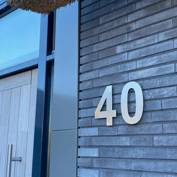 Een modern gebouw aan de buitenkant heeft grijze bakstenen muren, een houten deur met metalen handvat en een groot huisnummer van 20 cm dat op de muur is bevestigd.