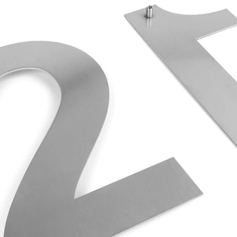 Close-up van twee grote Adamo RVS 20cm huisnummers van yessential.nl op een witte achtergrond: op de ene staat gedeeltelijk "2" en op de andere "1", met een zichtbare bevestigingspin voor een elegant zwevend effect.