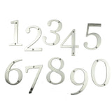 De Matteo Nickel 10cm huisnummers van yessential.nl, in metallic zilver met een geborstelde afwerking en voorgeboorde gaten voor eenvoudige montage, zijn gerangschikt van 0 tot 9 op een witte achtergrond.