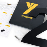 De Adamo Black 20cm van yessential.nl bevat een zwart metalen nummer 2, installatiemateriaal, instructies en een zwarte map met een geel yessential logo - perfect voor iedereen die moderne huisnummers wil.