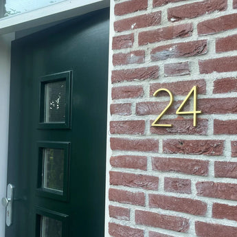 Een donkergroene deur met drie kleine ramen staat naast een rode bakstenen muur, met huisnummer 24 in Amato Gold 15cm cijfers van yessential.nl.