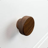 De Arriero Walnut knop van yessential.nl is stijlvol gemonteerd op een wit kast- of ladefront met structuur, met een subtiele opstaande rand zichtbaar op de achtergrond.