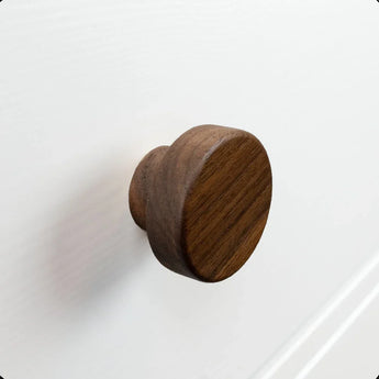 De Arriero Walnut knop van yessential.nl is stijlvol gemonteerd op een wit kast- of ladefront met structuur, met een subtiele opstaande rand zichtbaar op de achtergrond.