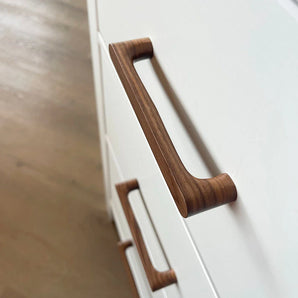 Close-up van twee Salgado Walnut handgrepen van yessential.nl, met een gladde afwerking, gemonteerd op witte kastladen met een lichte houten vloer op de achtergrond.