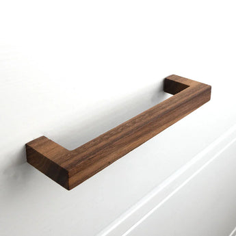 De Vasco Walnut ladegreep van yessential.nl, met een modern minimalistisch rechthoekig design, is bevestigd aan een witte kastdeur.