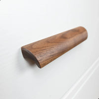Een close-up van Lucasso Walnut handgrepen van yessential.nl, met een glad, gebogen ontwerp op een wit ladefront - ideaal voor een natuurlijke inrichting.