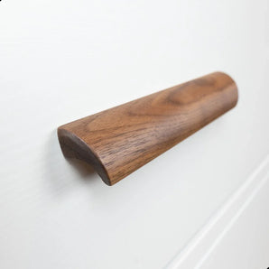 Een close-up van Lucasso Walnut handgrepen van yessential.nl, met een glad, gebogen ontwerp op een wit ladefront - ideaal voor een natuurlijke inrichting.