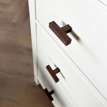 Close-up van de Vasco Walnut dressoir van yessential.nl, met witte lades met handgrepen van donker walnotenhout, getoond vanuit een schuin bovenaanzicht tegen een houten vloer.