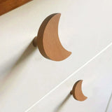 Two Bambino Moon houten meubelknop handgrepen van yessential.nl, gevormd als maansikkels, zijn bevestigd aan een witte commode-perfect voor een speels accent in elke kinderkamer.