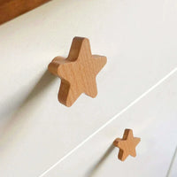Twee Bambino Star houten knoppen van yessential.nl zijn bevestigd aan een witte commode, met één knop dichter bij de camera - een ideale manier om charme en stijl toe te voegen aan elke kinderkamer knopjes collectie.