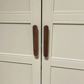 Een paar Arriero Walnut kastdeuren van yessential.nl heeft verticale houten handgrepen die dicht bij elkaar in het midden zijn geplaatst, waardoor een optische illusie ontstaat die doet denken aan een bruine hotdog.