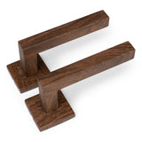 De Domaso Walnut Set van yessential.nl bestaat uit twee moderne rechthoekige deurklinken in donker hout met een vierkante basis, naast elkaar op een witte achtergrond.