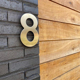 Een Adamo RVS 15cm metallic nummer 8 van yessential.nl is gemonteerd op een donkere bakstenen muur naast een houten paneelmuur.