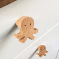Two Bambino Octopus houten meubelknoppen van yessential.nl met een simpel, minimalistisch ontwerp zijn bevestigd aan een wit kastje - perfect voor een speels accent in de kinderkamer.