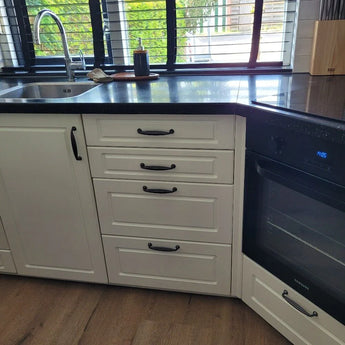 De Alvaro Black keuken van yessential.nl heeft witte kastjes, antraciet grijze afwerking, een ingebouwde oven, roestvrijstalen gootsteen, zwart aanrechtblad, klassieke handgrepen en ramen boven het aanrecht voor natuurlijk licht.