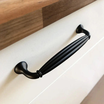 Een close-up van de Alvaro Black Knob van yessential.nl, met een gegroefd ontwerp, geïnstalleerd op een witte lade onder een houten aanrechtblad.