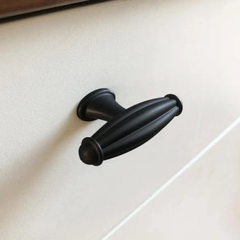 Een close-up van de Alvaro Black meubelknop van yessential.nl, met een zwarte, ovale vorm met geribbeld design en antracietgrijze afwerking, gemonteerd op een witte kastlade.